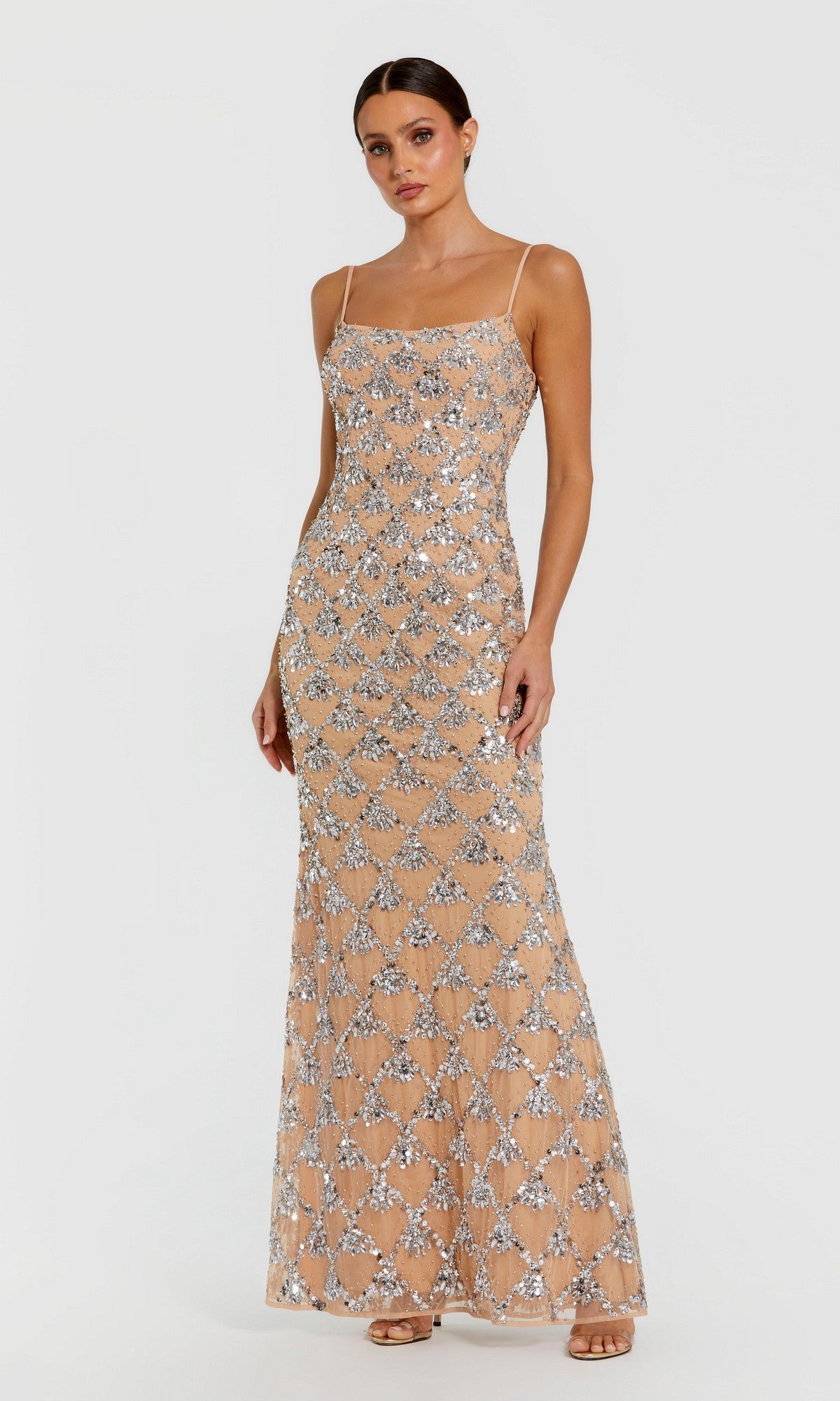 A woman wearing the Mac Duggal 94184 long formal dress in silver, featuring floor-length geometric sequin patterns and thin straps, stands against a plain light background.